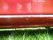 1993 Mazda MX-3 - Close-up view of a red car's side skirt, showing rust and a screw attachment.