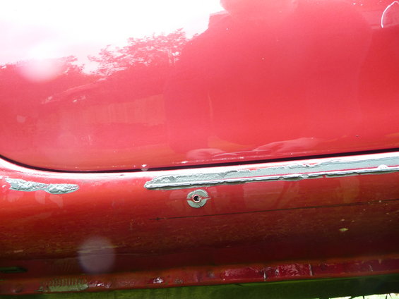 Red car side skirt with peeling paint and a circular mounting point