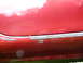 1993 Mazda MX-3 - Close-up view of a red car's side skirt, showing wear and tear on the trim and a visible mounting hole.