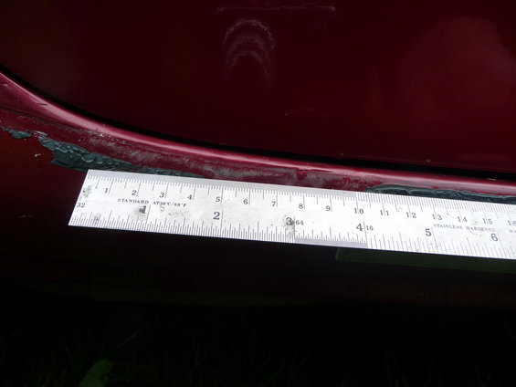 Red car side skirt detail with ruler measuring gap