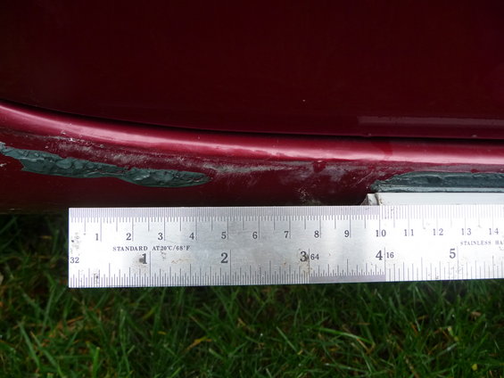 Close-up of a car's lower door edge and rocker panel with a ruler measuring the damage
