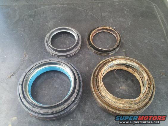 Two new wheel bearing seals and two old, worn-out ones on a dark surface