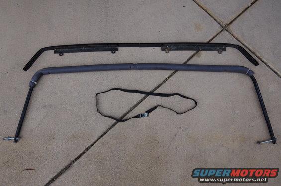 Car roll bar and a black trim piece laid out on concrete. A black strap is also visible