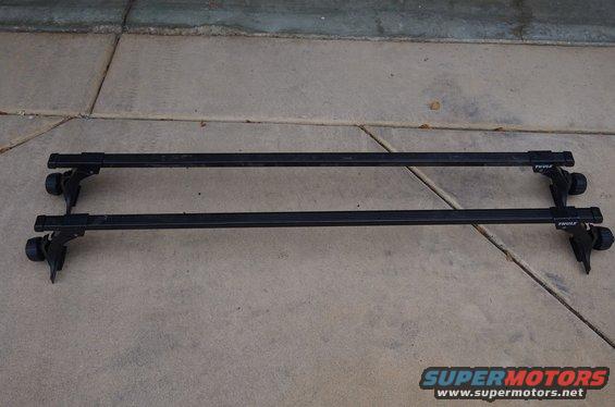 Pair of black Thule roof rack crossbars with mounts on concrete
