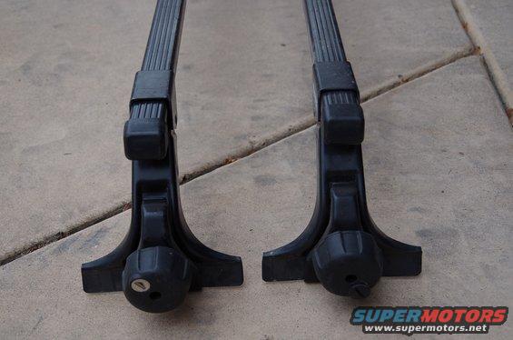 Two black roof rack feet with locking mechanisms on a concrete surface
