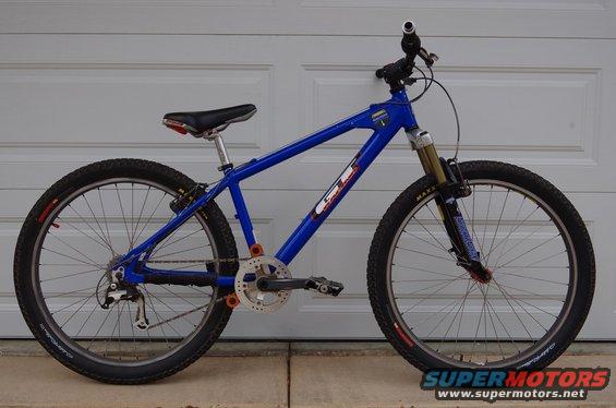 Blue GT mountain bike parked in front of a garage door. It has knobby tires and front suspension