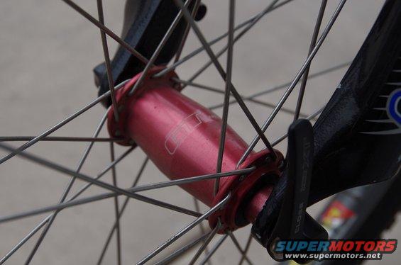 Close-up of a red bicycle wheel hub with spokes and a quick-release lever. Text on lever says 'CLOSE'