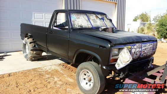 Black pickup truck with large rear tires, hood scoop, and newspaper-covered windows