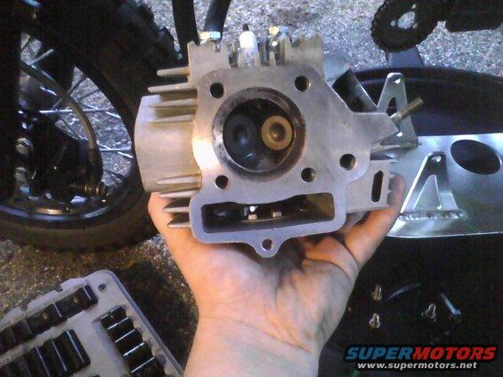 Hand holding a motorcycle engine cylinder head with valves visible inside