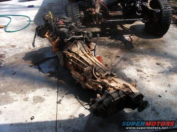 Engine and transmission assembly on concrete, with vehicle frame in background