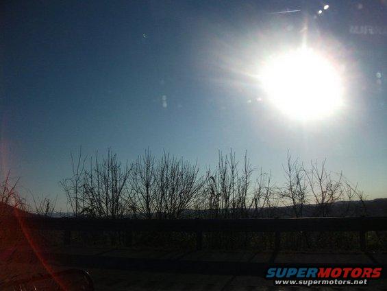 Sunny sky over silhouetted trees and a guardrail
