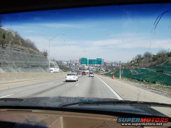 Dashboard and windshield view from a vehicle on a highway with traffic and city skyline in the distance