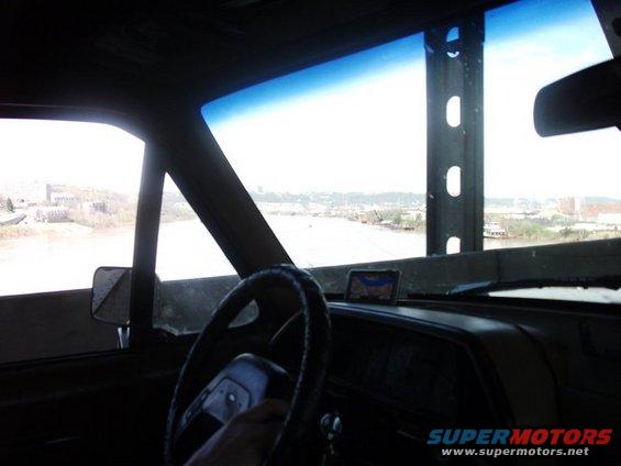 Interior view from driver's seat, looking out windshield at a river and distant buildings