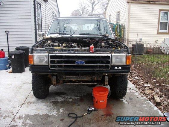 Ford truck with hood open, engine exposed, parked in driveway with tools nearby