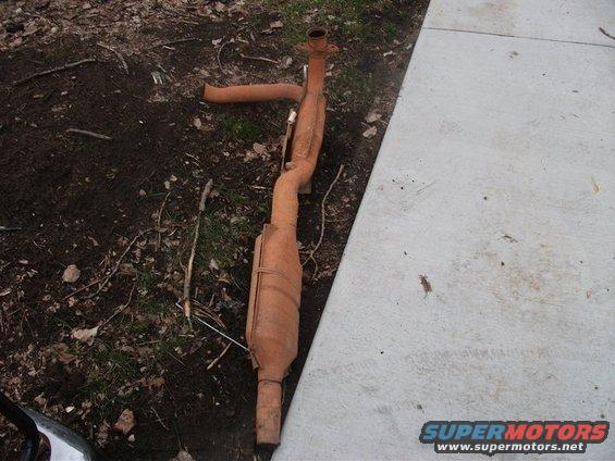 Rusty exhaust pipe and catalytic converter on the ground next to a concrete path