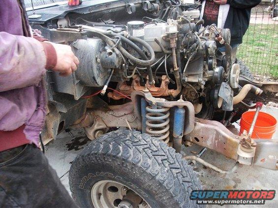 Truck engine bay with front suspension and tire visible. "SUPERMOTORS" text at bottom right