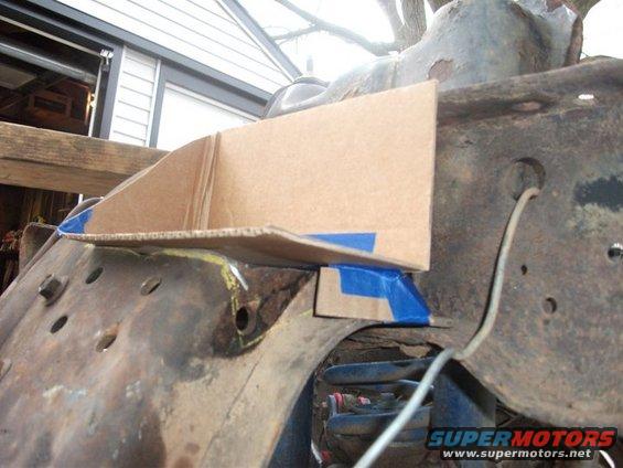 Cardboard template on rusty vehicle frame with blue tape, showing suspension components