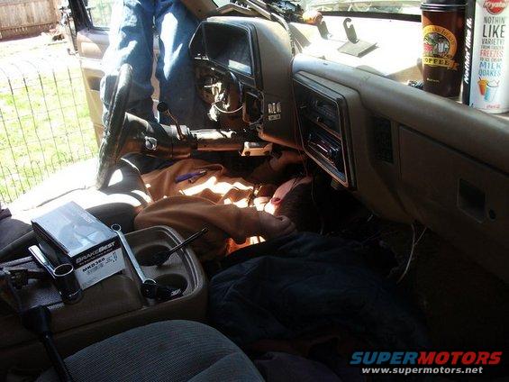 Person working on dashboard wiring inside a vehicle. Tools and parts are on the console