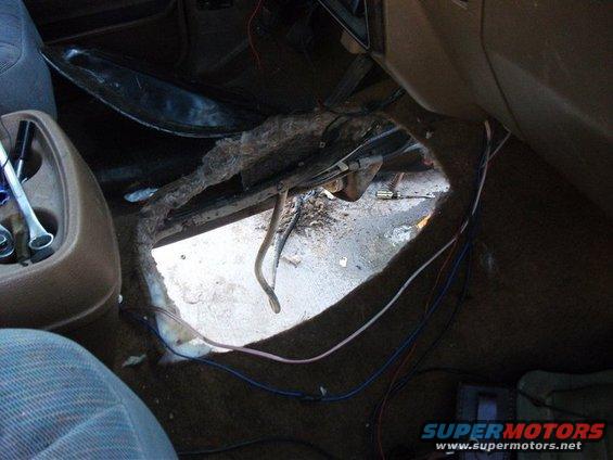 Interior floor of a vehicle with a large hole, exposed metal, wiring, and tools visible