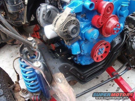 Engine block painted blue with red accessories, turbocharger, and alternator. Blue coil spring suspension visible