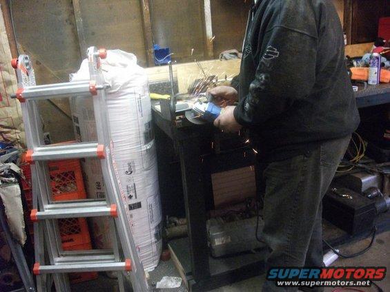 Person using an angle grinder in a workshop with a ladder and large bag