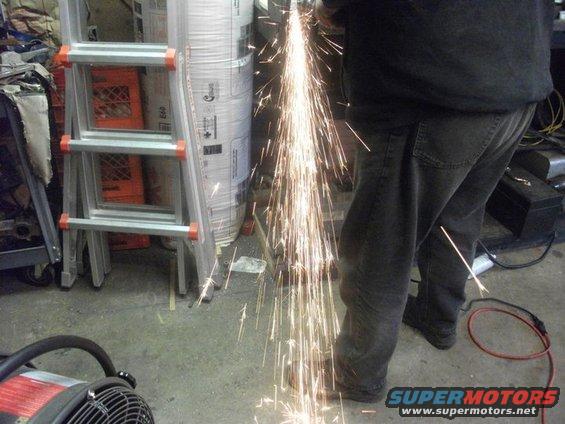 Person using an angle grinder, creating a shower of sparks. Ladder and building materials in background