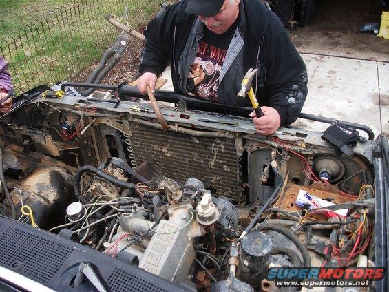Man working on engine bay, front view. Some text visible on engine block