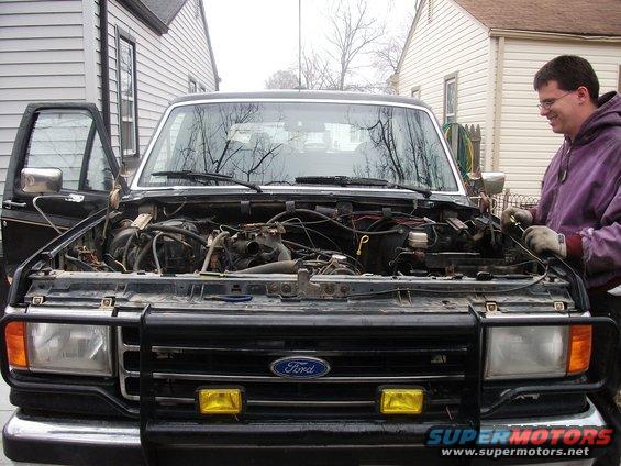 Black Ford Bronco with hood open, showing engine compartment and a man working on it