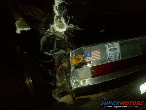 Rear of a damaged vehicle with an American flag sticker and a 'Built Ford Tough' sticker