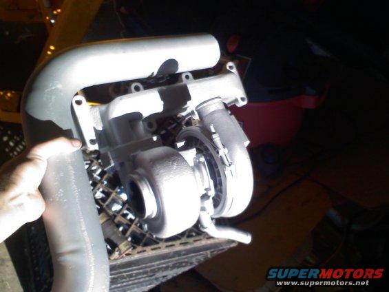 Turbocharger assembly with intake piping held by a hand, resting on a metal grate