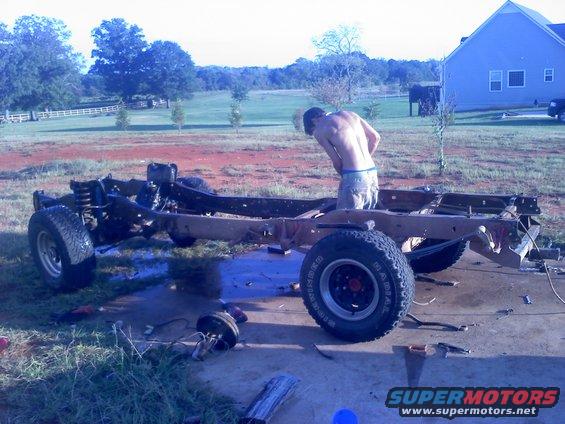 guy working on bare truck frame with wheels and suspension parts scattered around