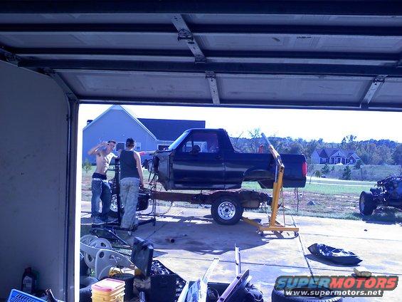 Black Ford Bronco body on a trailer, missing front end, being worked on by two people