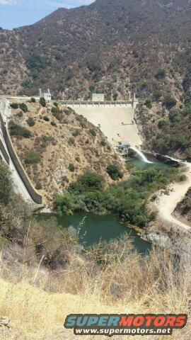 Dam and reservoir with water flowing, dry hillsides, and a "SUPERMOTORS" watermark