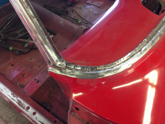 Close-up of red car's interior showing chrome trim and bare metal floor during restoration