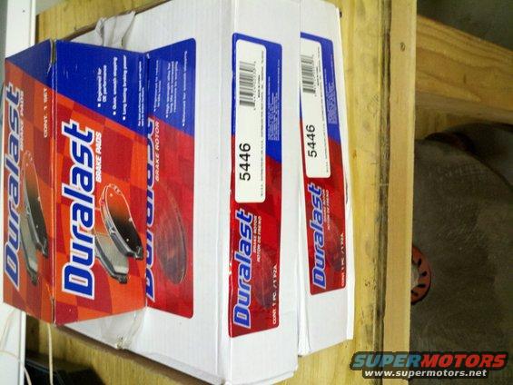 Boxes of Duralast brake pads and rotors stacked on a wooden shelf