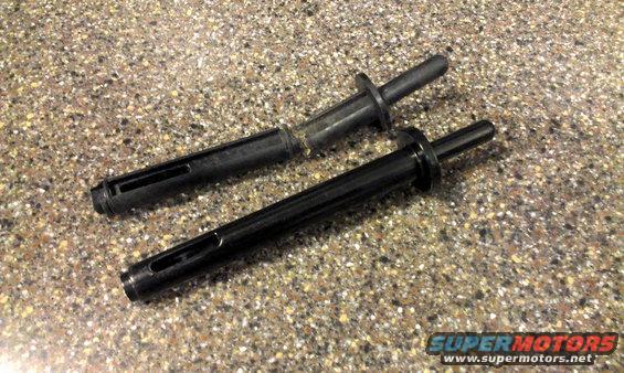 Two black plastic parts with protruding pins and slotted bodies on a speckled surface