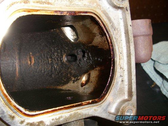 Close-up of a heavily carbon-fouled engine intake manifold port with oil residue