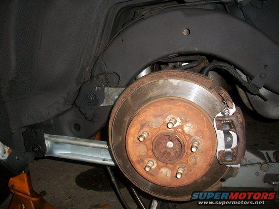 Rear brake assembly of a 2001 Ford Crown Victoria, showing a rusty rotor and caliper, supported by an orange jack stand