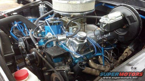 Engine bay showing V8 engine with blue spark plug wires, chrome valve covers, and headers
