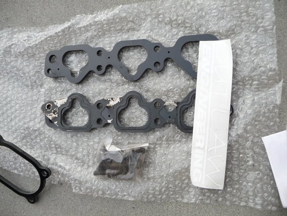 Engine intake manifold gaskets and a bag of hardware on bubble wrap. White sticker with text is visible