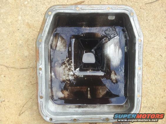 metal oil pan filled with dark, sludgy fluid and some debris