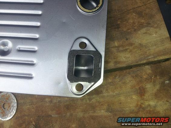 Metal oil cooler plate with gasket and bolt holes on a wooden surface