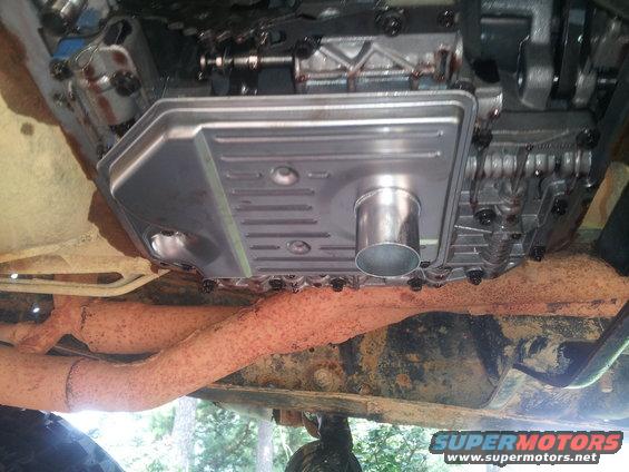 Underside view of a transmission pan and rusted exhaust pipe