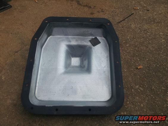 Transmission oil pan with gasket, sitting on concrete. Some debris on the ground
