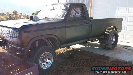 Modified pickup truck with large paddle tires on rear, hood scoop, and taped windows