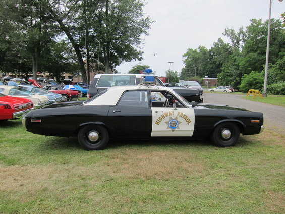 Black and white police car with 'HIGHWAY PATROL' on the door. Other cars are parked in the background