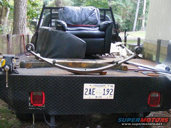 Leaf spring on a flatbed truck, with a recliner chair in the background. Mississippi license plate 2AE 192