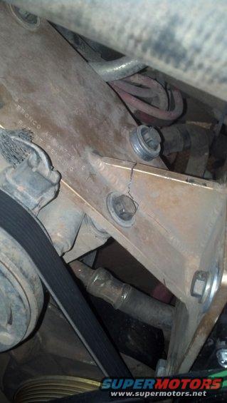 Cracked metal bracket with bolts and a belt near engine components