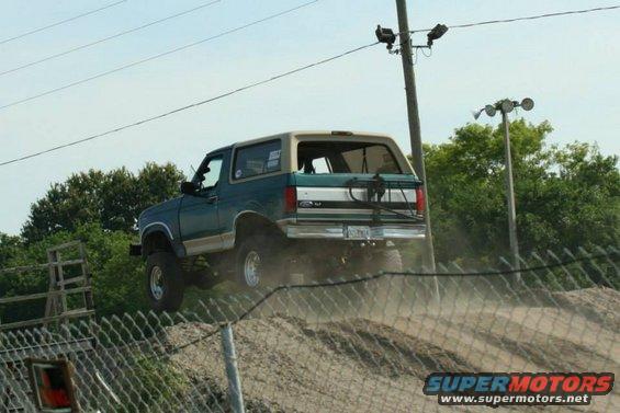 Green and tan Ford Bronco driving up a dirt hill, rear view