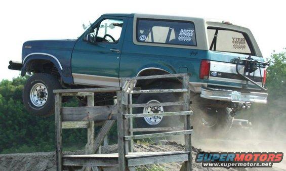Teal and tan 1996 Ford Bronco driving over a wooden obstacle